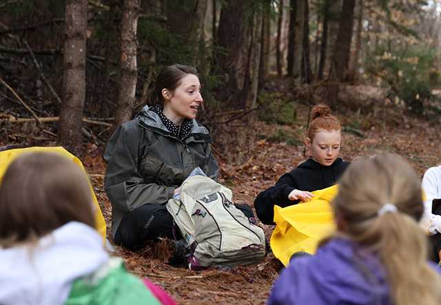 A teacher and middle school aged students sit in a circle in a forest
