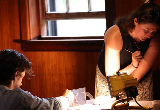 Two people study a tabletop solar model in a dim room