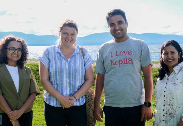 Four adults pose in front of Lake Champlain and the Adirondack mountains in summertime