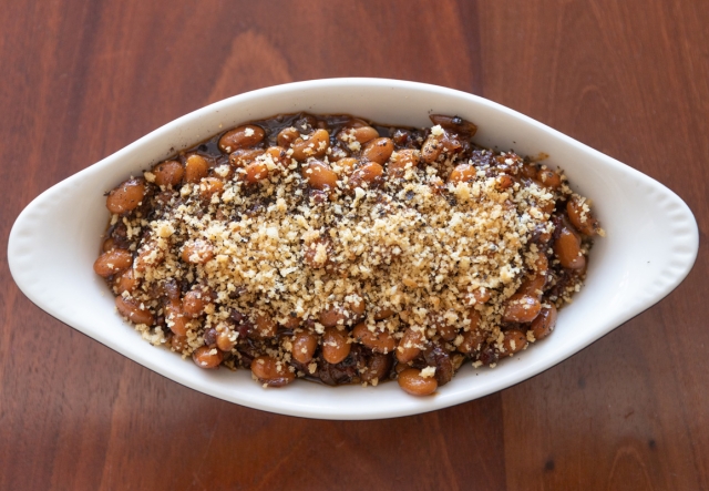 A dish filled with Maple Black Pepper Baked Beans, topped with breadcrumbs.