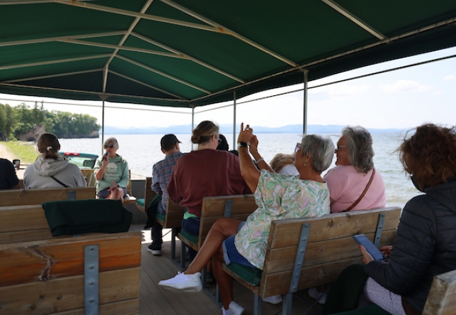 an open-air tour wago full of people looking towards their guide with lake in the background