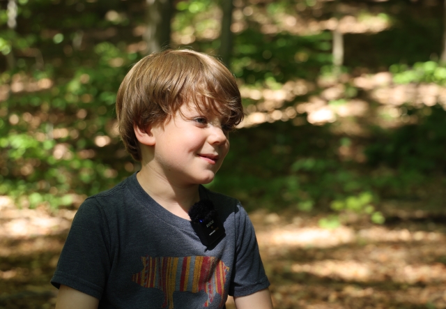 A young boy smiles in a forested setting.
