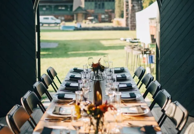 long table set with dishes, flowers, chairs inside a room looking out through open doorway to lawn