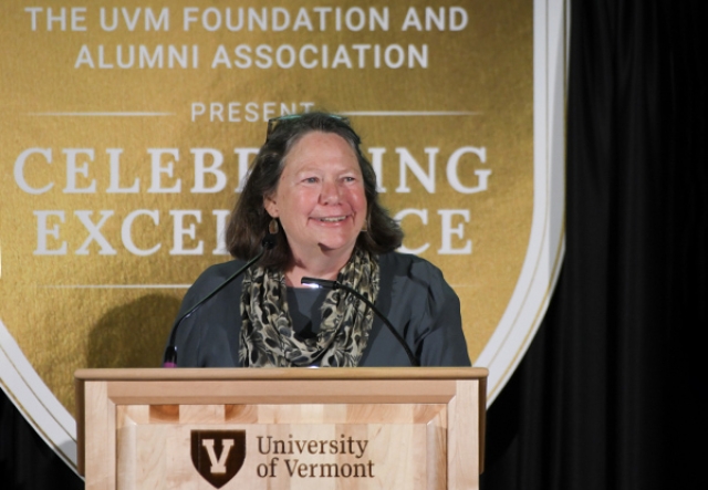 megan camp, with shoulder length brown hair, stands at a podium
