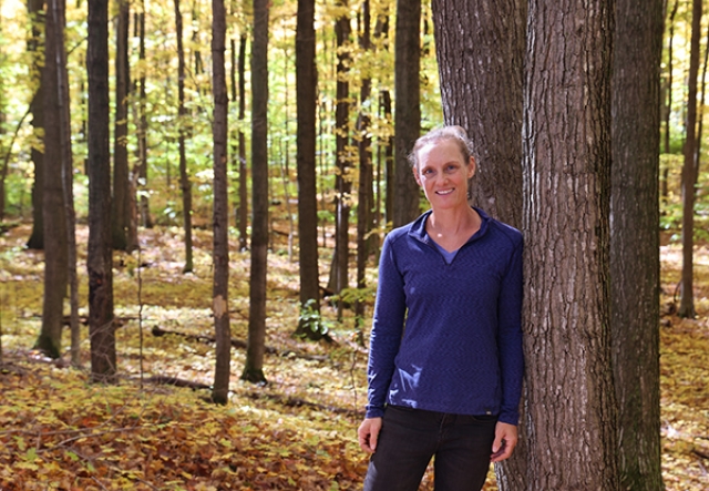 woman leaning against a tree with yellow forest behind her