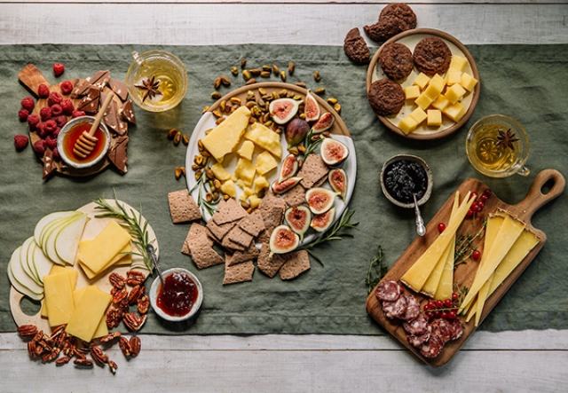 table with green runner full of plates of cheese and pairings: figs, nuts, jams, fruit