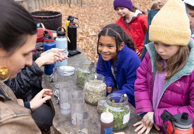 A group of young children make tea at an outdoor table