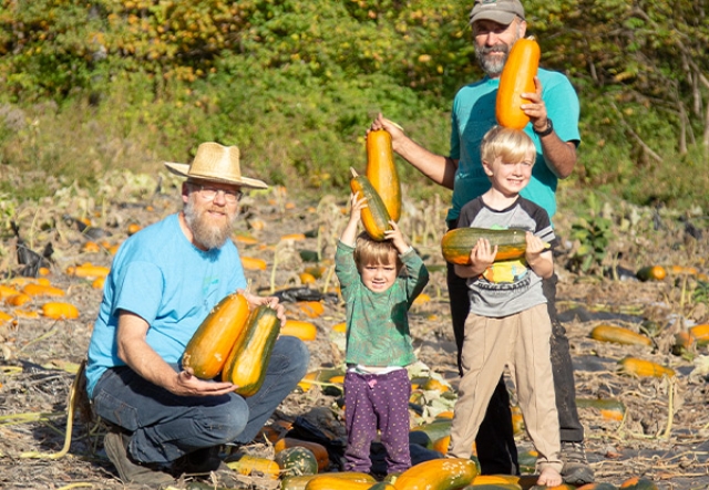Two adults and two children in a squash patch.