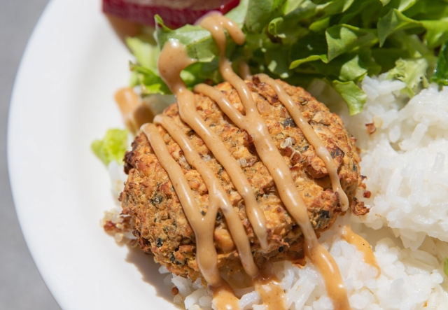 A plate of food featuring a falafel patty drizzled with a sesame dressing sauce, served on a bed of white rice a fresh green salad.