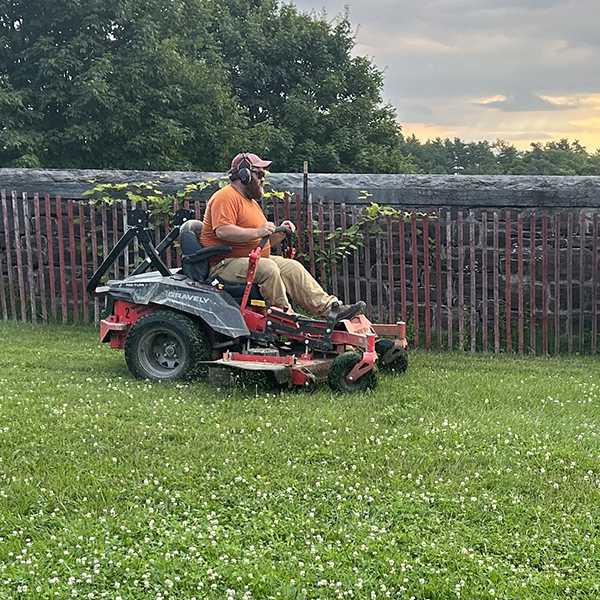 bearded man driving an electric mower with stone wall in background