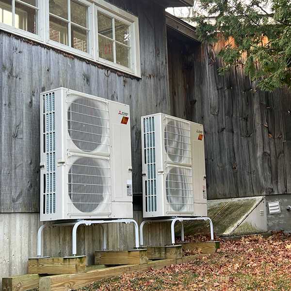 two heat pumps installed along wooden sided exterior wall of a house.