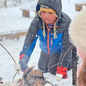 A young boy roasts a marshmallow over a campfire in winter