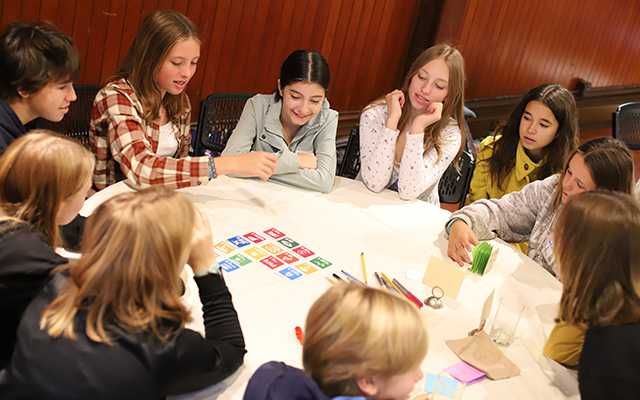 A group of middle school aged students sits around a table sorting colorful cards
