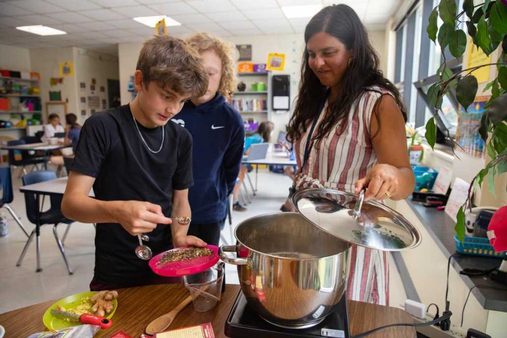 A teacher and a student mix loose leaf tea into a simmering pot