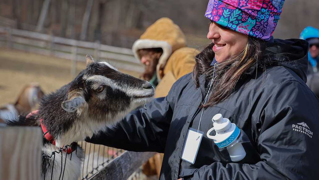 A woman smiles while petting a goat over a fence