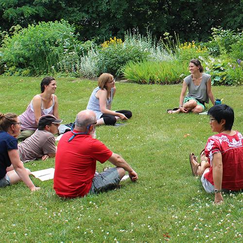 Educators sit in a circle in the grass, talking, during a leadership academy gathering