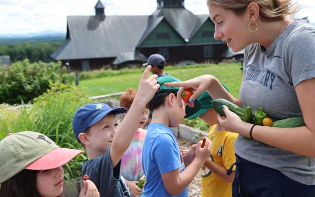 a summer camp educator looks at a garden harvest with campers