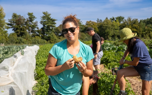 A woman smiles holding a heart shaped potato on a farm