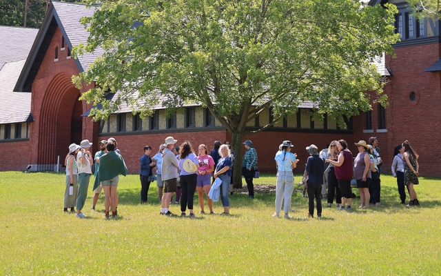 Thirty people stand in a circle outside of a large brick building