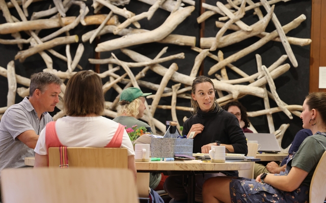 Small groups of people sit around tables in discussion in a large gathering space