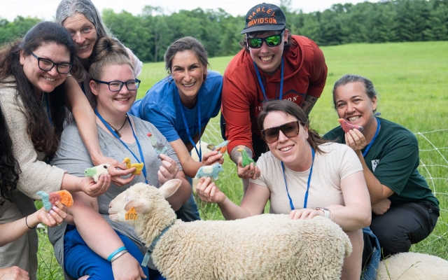 Educators gather around a lamb, smiling and holding felted figurines.
