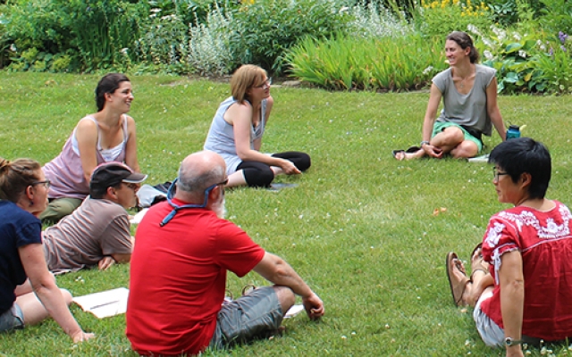 Educators sit in a circle in the grass, talking, during a leadership academy gathering