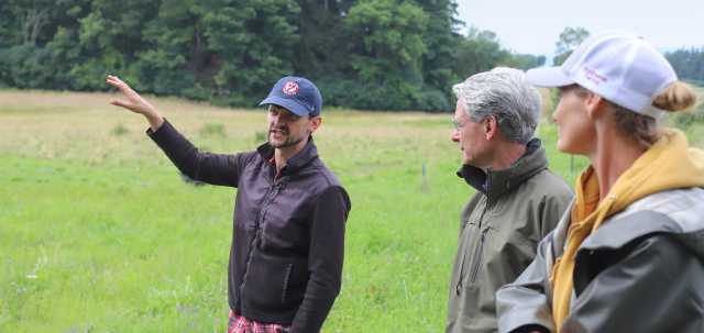 man in field in blue hat talking with two others