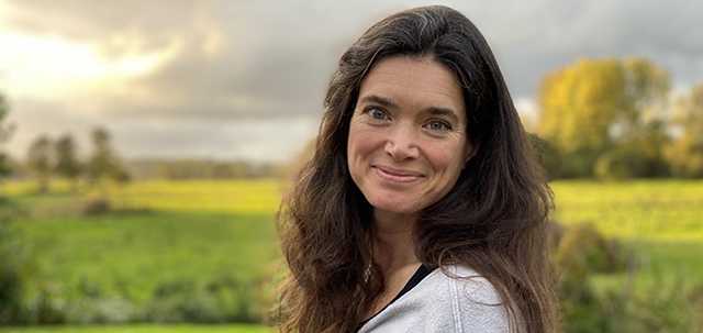 Woman with long dark hair with green sunny fields in background
