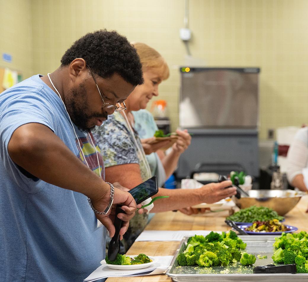 Two educators prepare broccoli and other food in a school cafeteria kitchen.