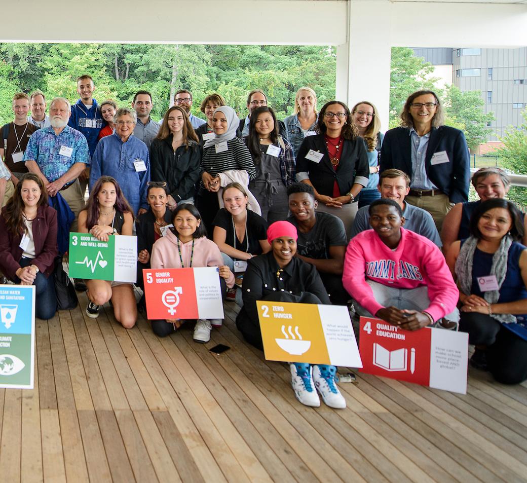 A large group of students, educators, and partners at Burlington's Sailing Center patio pose with Sustainable Development Goal posters while smiling.