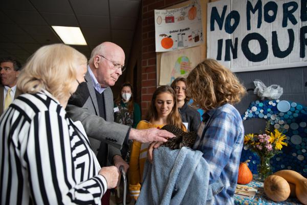 Senator Patrick Leahy and Marcelle Pomerleau Leahy talk with Crossett Brook Middle School students during the Farm to School Project Share. Here they speak with students from the sustainability club and meet Molly the hen, part of the school's flock of chickens. 