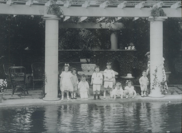 A pergola is basically an arbor that forms a shaded walkway, passageway, or sitting area. Pillars usually hold up cross-beams and a lattice that supports woody vines. Here, Lila and Sewardâs grandchildren pose under the pergola (note pergola wall in back). (L to R): Electra, Derick, Sam, William Seward III, Seward Webb Pulitzer, Frederica, Lila, and Osborn. Aileen Webb is hiding behind the pillar. ca. 1916 (Shelburne Farms Archives).