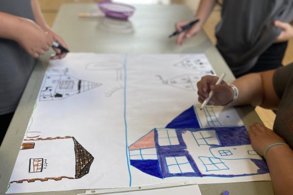 Students draw their ideal neighborhoods with markers on large sheets of paper