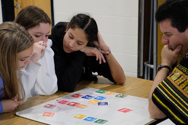 Three students sit with teacher around sustainable development goal cards