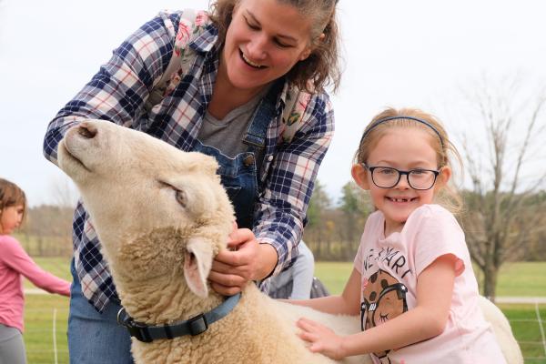 A young student and chaperone meet a sheep outside the Shelburne Farms Farm Barn during a school program