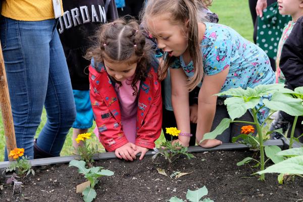 Two young students look in awe at flowers planted in school garden