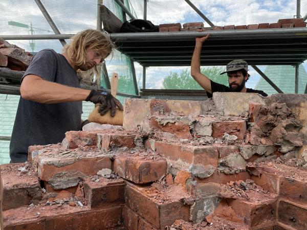 Men on staging cleaning and dismantling chimney bricks.