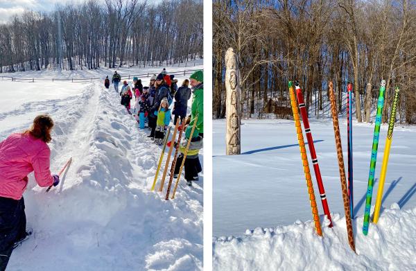 a child pushes a decorated stick - a snow snake - down a snow chute, while others look on.