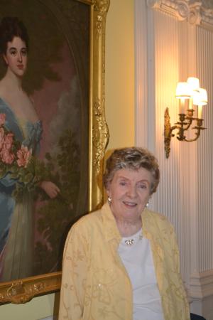 Volunteer Shirley Murray standing in front of portrait painting of Lila Vanderbilt Webb