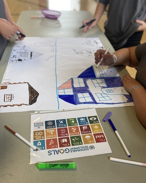 Georgia Middle School students hit the ground running on day one of a year-long sustainable development project. Small groups worked together to share and design their ideal communities, inspired by the UN Sustainable Development Goals. Students draw with markers near paper that reads, UN Sustainable Development Goals