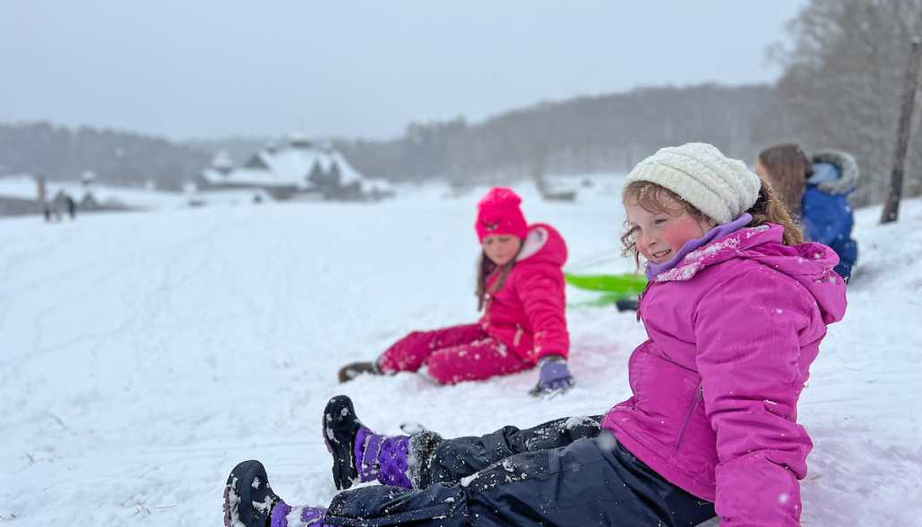 kids sit in the snow atop a hill