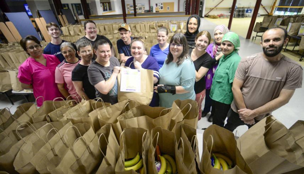 Group of school meals staff at a school cafeteria, standing behind rows of filled grocery bags.