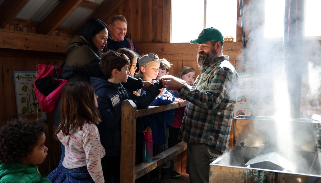 Person in sugarhouse gives a demo to a group of children and adults.