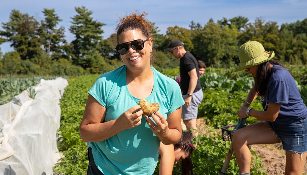 A woman smiles while holding a heart shaped potato in a potato field
