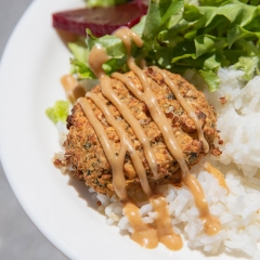 A plate of food featuring a falafel patty drizzled with a sesame dressing sauce, served on a bed of white rice a fresh green salad.
