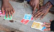A closeup of three sets of young peoples hands hovering over colorful cards spread over a wooden table