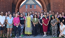 A large group of people smile under a brick archway