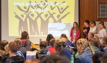 A small group of young people present to a large room in front of a screen