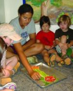 Teacher and young students gather around a tray of vegetables for the Plant Parts We Eat activity