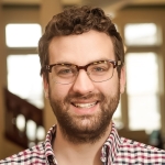 Elliot Franklin - dark curly hair with beard and glasses, wearing a checked shirt